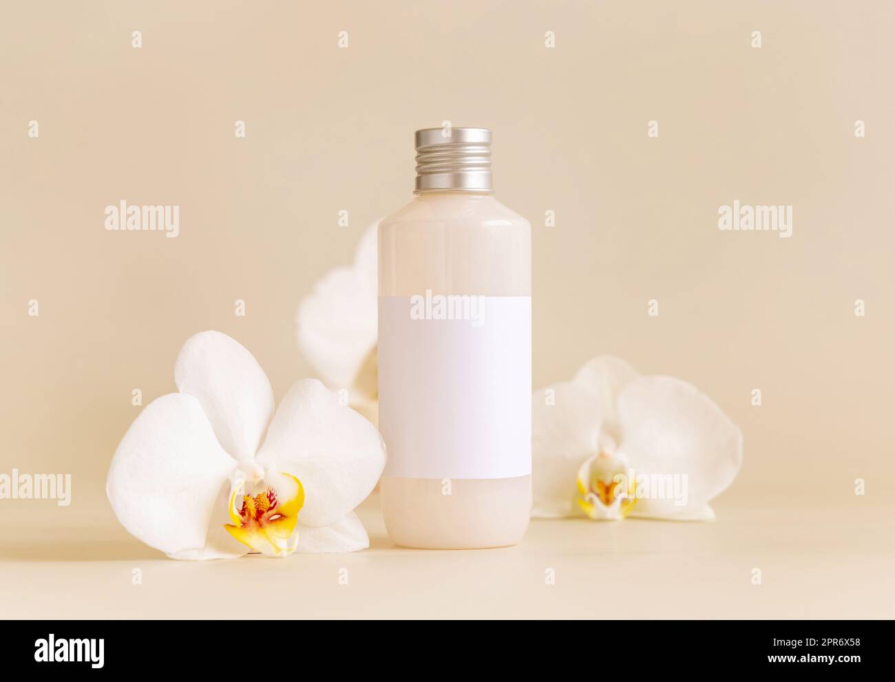 Kosmetikflasche mit leerem Etikett neben weißen Orchideenblumen auf hellgelbem Modell Stockfoto