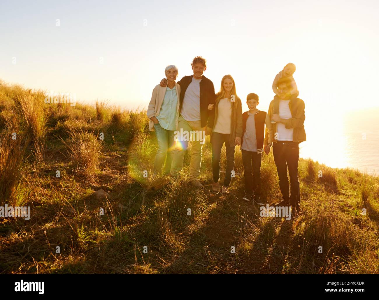 Sie sind am glücklichsten, wenn sie alle zusammen sind. Ein Porträt einer glücklichen Familie, die bei Sonnenuntergang auf einem grasbewachsenen Hügel steht. Stockfoto