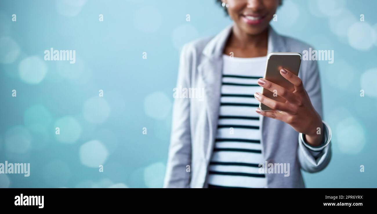 Machen Sie Kontakt und machen Sie es möglich. Beschnittene Studioaufnahme einer jungen Geschäftsfrau mit Mobiltelefon vor blauem Hintergrund. Stockfoto