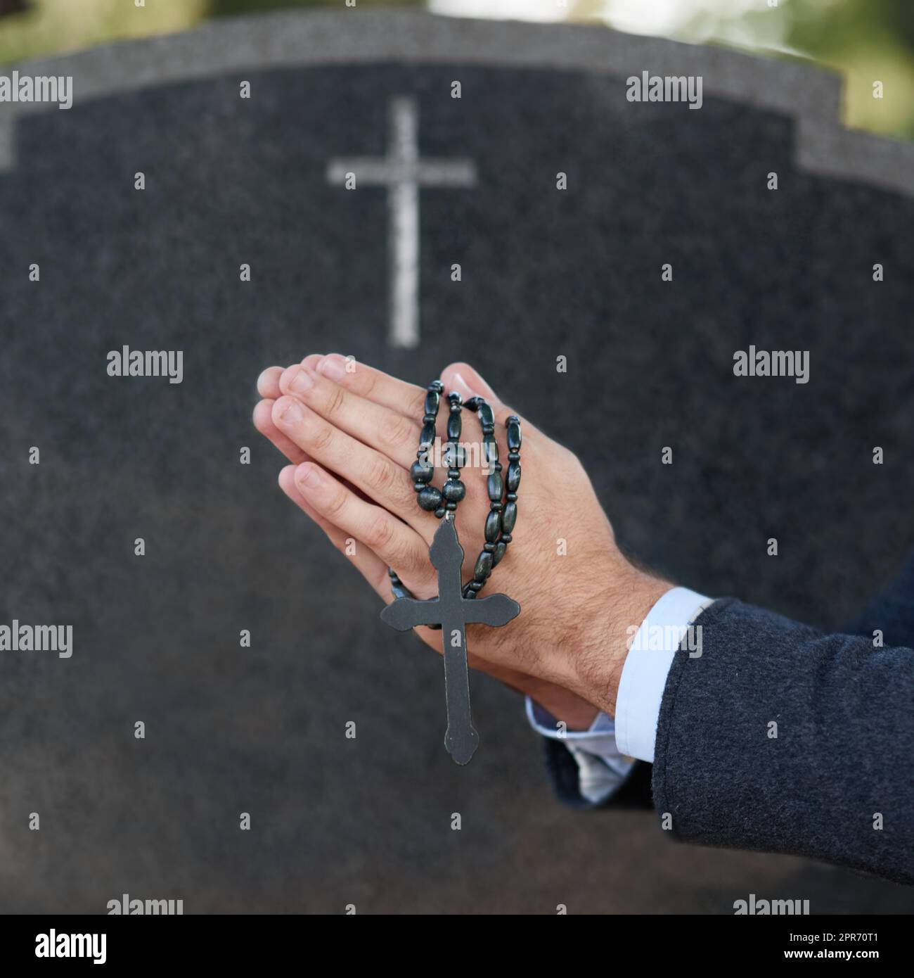 Betet für den ewigen Frieden. Ausgeschnittene Aufnahme eines Mannes, der mit einem Rosenkranz auf ein Grab betet. Stockfoto