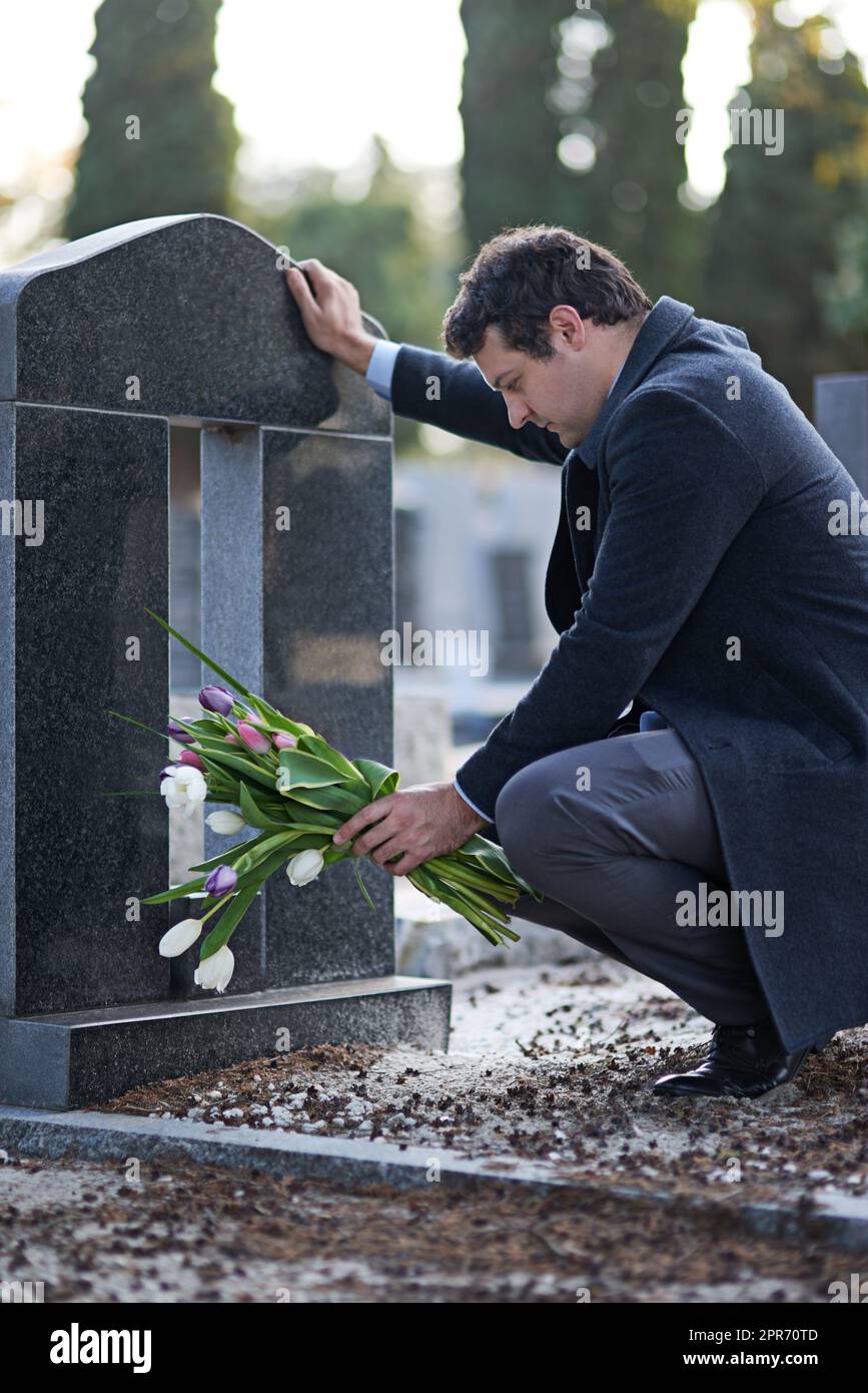 Sie waren ihre Lieblingsblumen. Aufnahme eines jungen Mannes, der eine Grabstätte mit einem Blumenstrauß besucht. Stockfoto