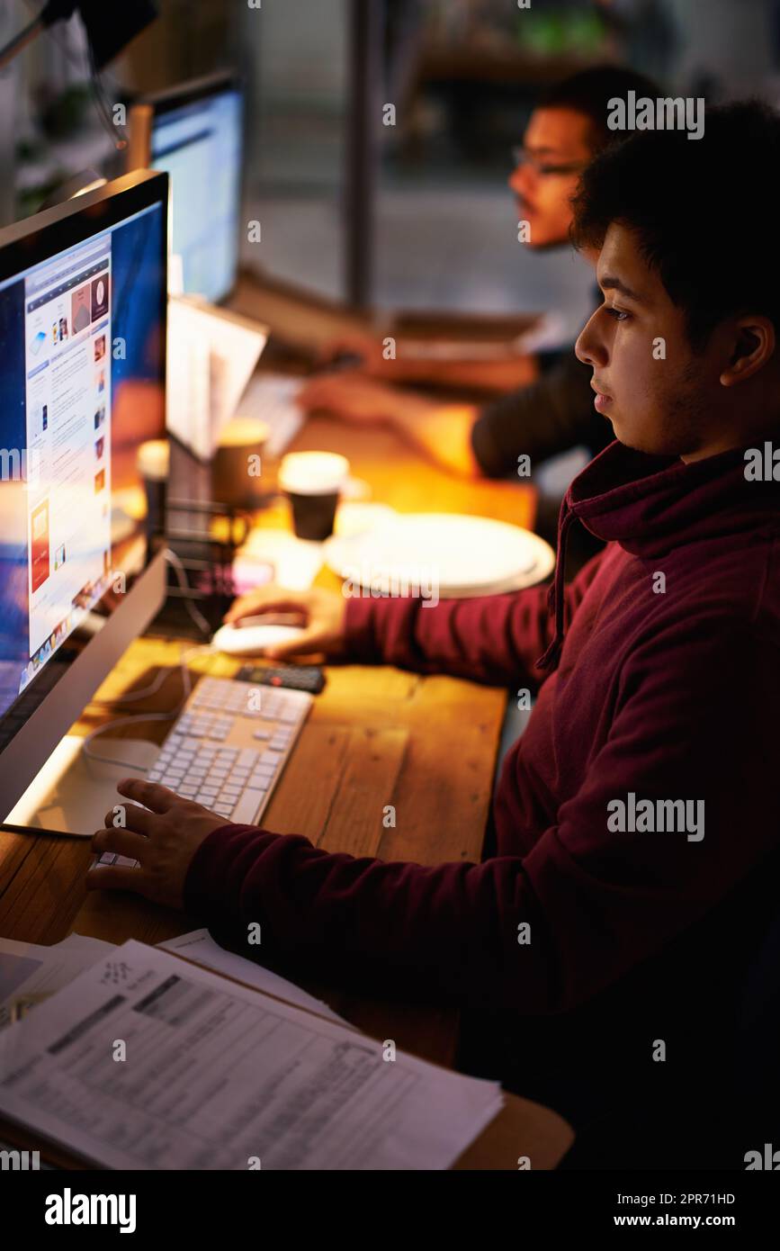 Die Arbeit erledigen. Eine kleine Aufnahme einer Gruppe junger Mitarbeiter, die in einem schwach beleuchteten Büro arbeiten. Stockfoto