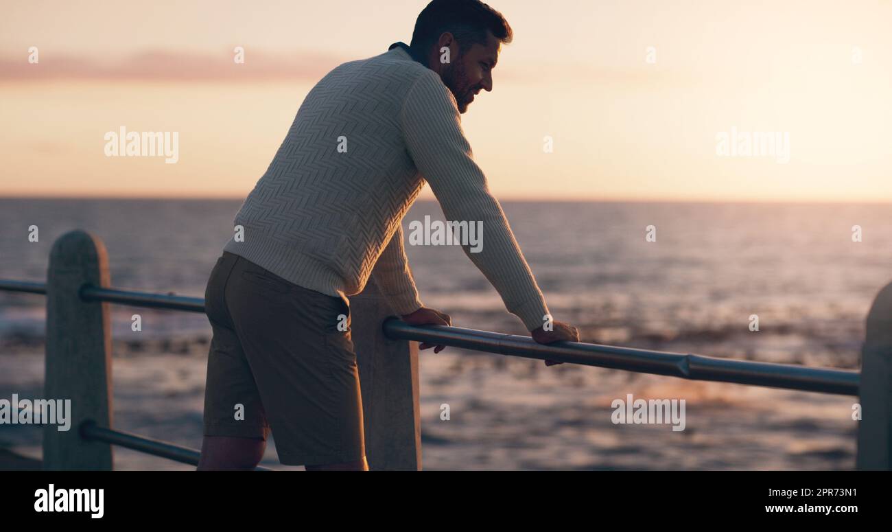 Beenden Sie einen langen Tag am Strand. Rückansicht eines Mannes, der den Sonnenuntergang am Strand beobachtete. Stockfoto