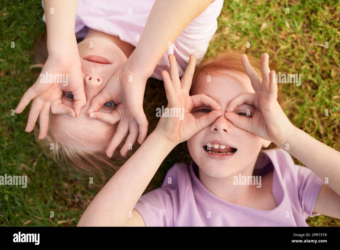 We Bis zum nächsten Mal. Zwei kleine Mädchen liegen auf dem Rücken und kreisen mit den Händen um ihre Augen. Stockfoto
