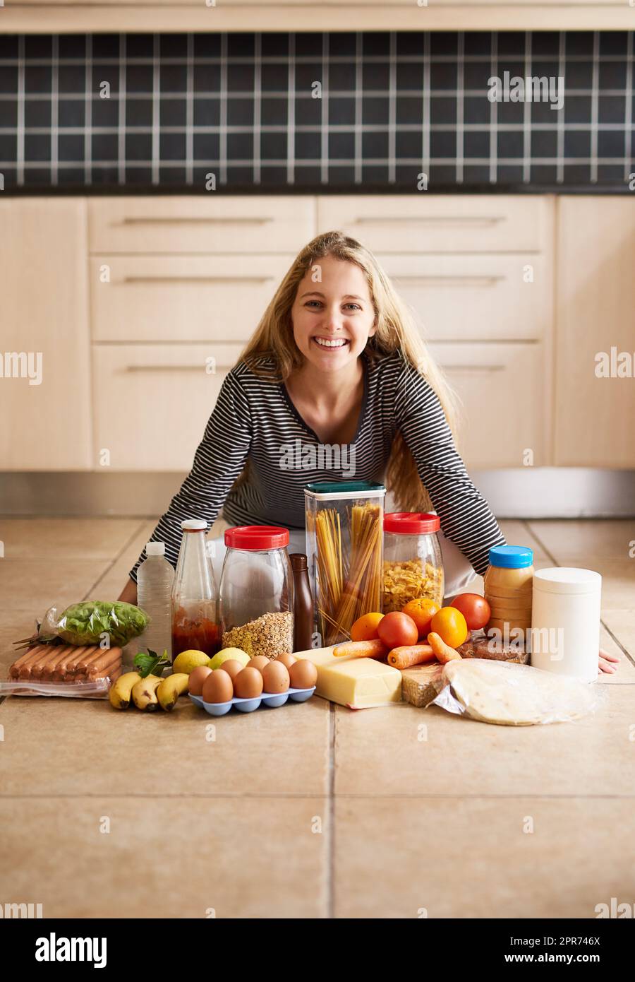 Alles, was ich für eine leckere Mahlzeit brauche. Aufnahme einer attraktiven jungen Frau, umgeben von verschiedenen Lebensmitteln in der Küche zu Hause. Stockfoto