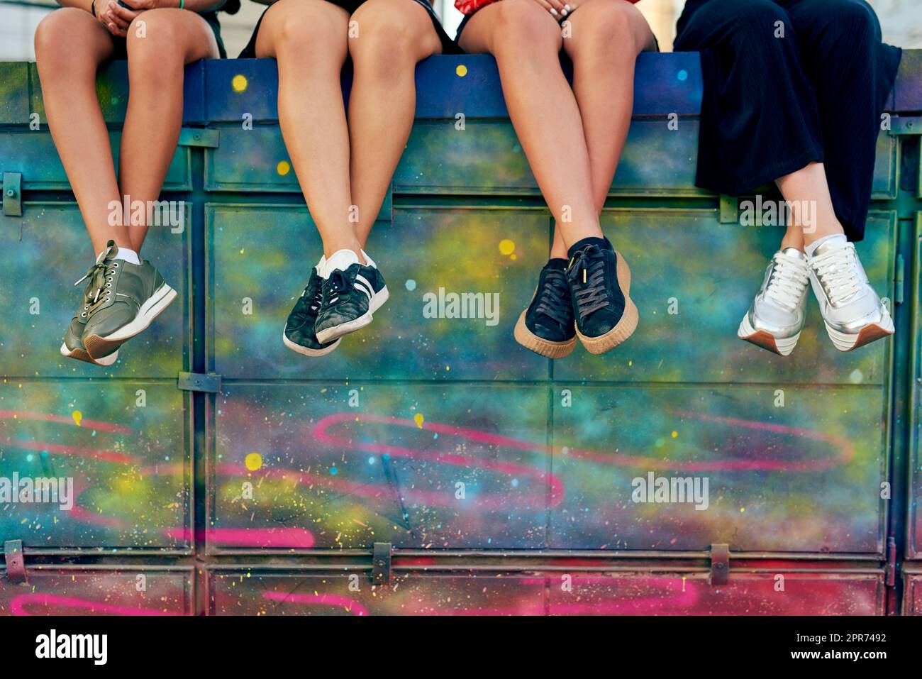 Nehmen Sie Platz. Zugeschnittene Aufnahme von vier unkenntlichen Freundinnen, die auf einer Graffiti-Wand in der Stadt sitzen. Stockfoto