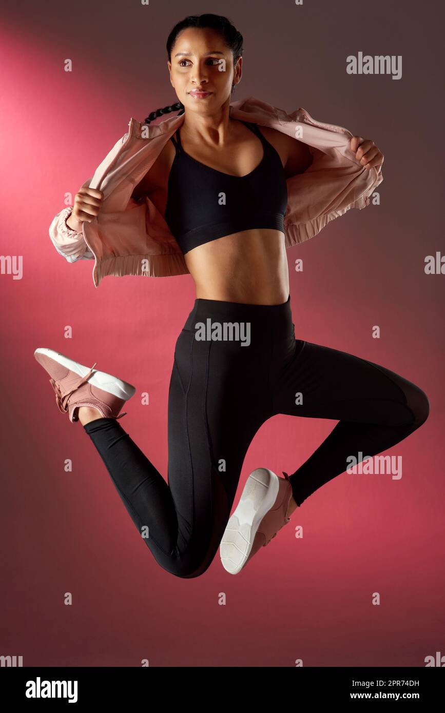 Ihr Körper ist so gut getönt. Studioaufnahme einer sportlichen jungen Frau, die vor rotem Hintergrund springt. Stockfoto