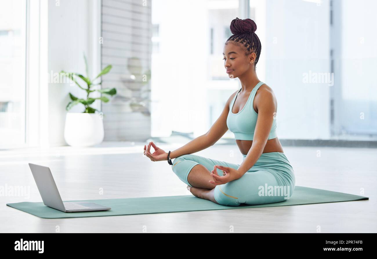 Die Bedeutung von Yoga online kennenlernen. Aufnahme einer attraktiven jungen Frau, die mit überkreuzten Beinen sitzt und einem Online-Yoga-Kurs folgt. Stockfoto