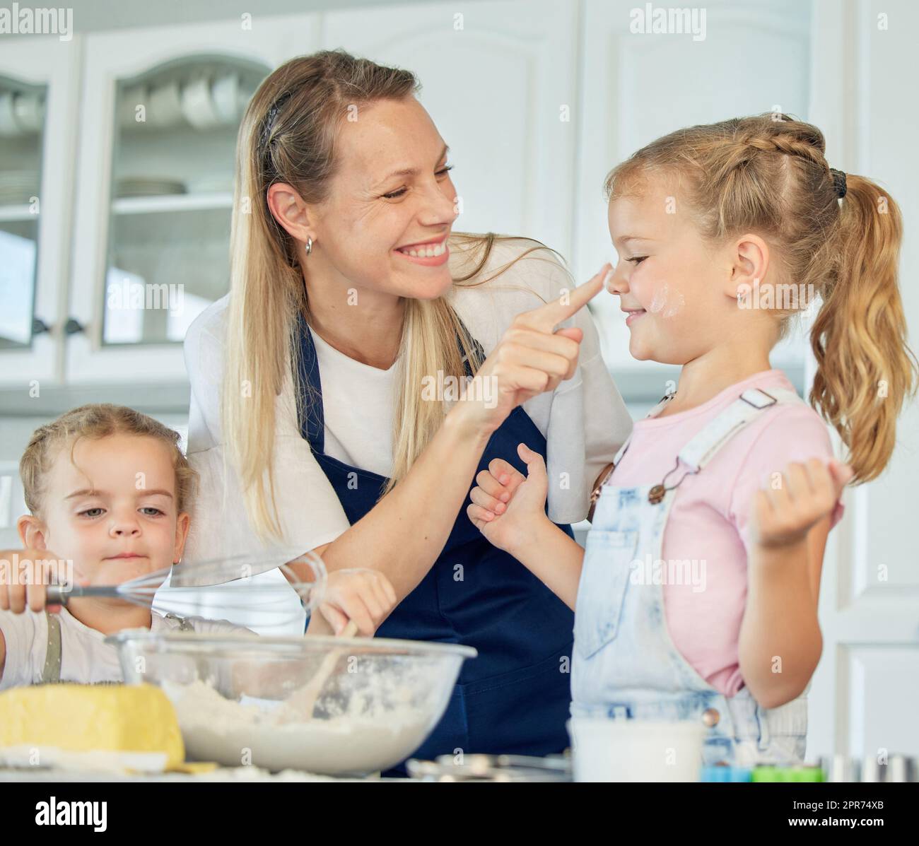 Glückliche, liebevolle Familie backen zusammen. Lächelnde Mutter und zwei Töchter kochen Kekse und haben Spaß in der Küche. Hausgemachtes Essen und ein kleiner Helfer. Stockfoto