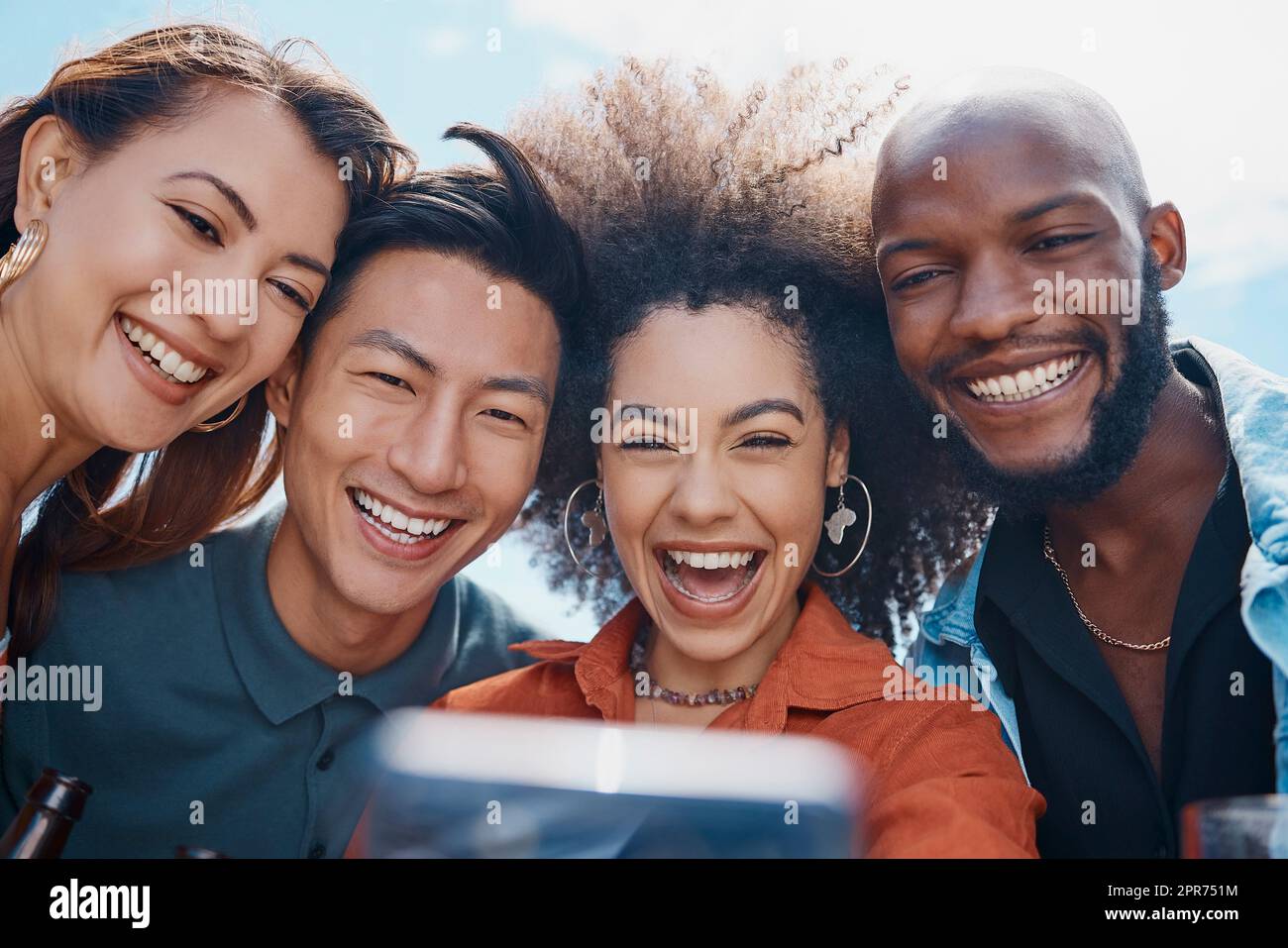 Eine Gruppe von Freunden, die ihr Handy benutzen, um Selfies zu machen, während sie sich draußen kennenlernen. Eine afroamerikanische Frau mit einem lächelnden Afro, die Fotos mit ihrer Clique für soziale Medien macht. Millennials, die Technik nutzen Stockfoto