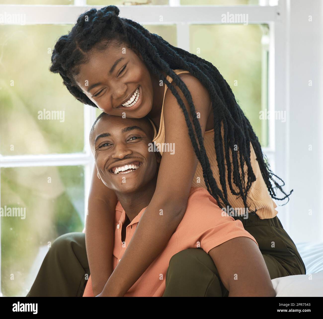 Ein junges schwarzes afroamerikanisches Paar lächelt und lacht, während sie sich liebevoll im Schlafzimmer zu Hause umarmen. Ein liebevoll aussehender Mann und eine liebevoll aussehende Frau, die Zeit miteinander verbringen und sich verlieben Stockfoto