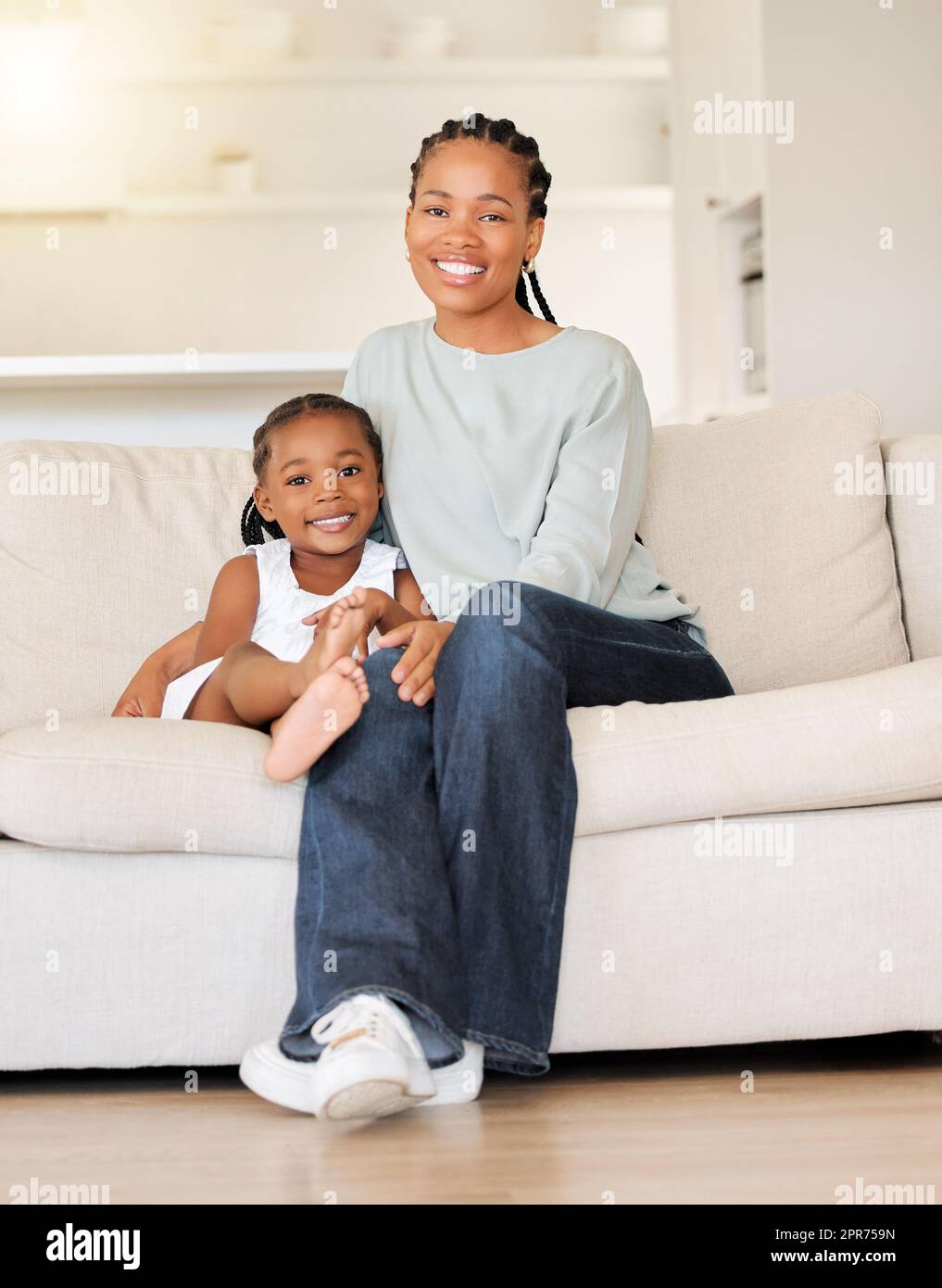 Glückliche und zufriedene junge afroamerikanische Mutter, die sich zu Hause auf der Couch in der Lounge entspannt und eine Beziehung zu ihrer kleinen Tochter herstellt. Ein kleines Mädchen lächelt, während es die Zeit mit ihrer mutter genießt Stockfoto