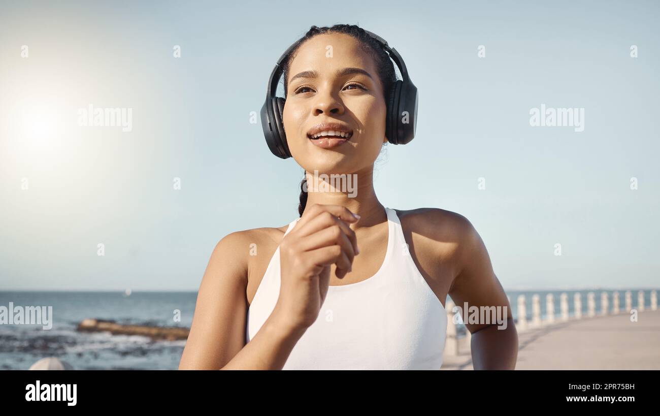 Glückliche junge Fitnessfrau in Sportbekleidung, die kabellose Kopfhörer trägt und Musik hört, während sie auf der Promenade joggt. Bewegung ist gut für Ihre Gesundheit und Ihr Wohlbefinden Stockfoto