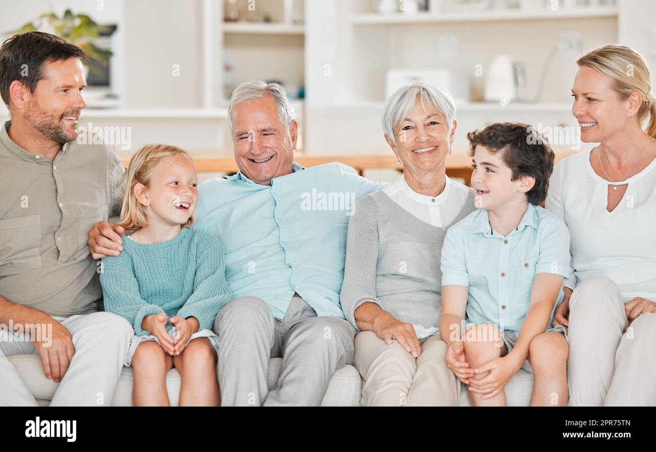 Sie besuchen gerne ihre Großeltern. Eine kurze Aufnahme von zwei entzückenden kleinen Kindern, die zu Hause mit ihren Eltern und Großeltern auf dem Sofa sitzen. Stockfoto