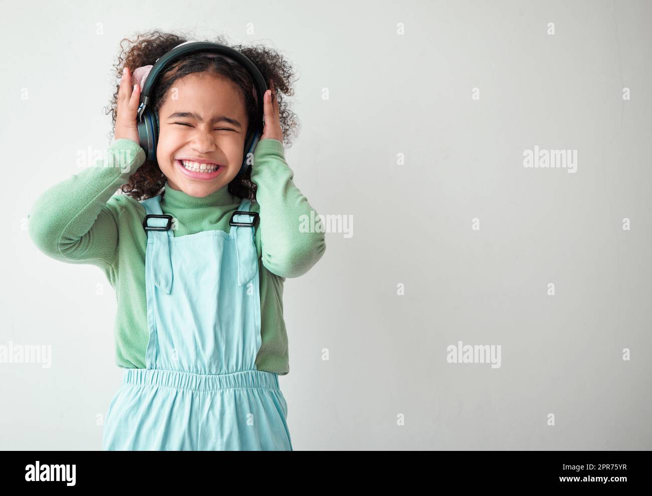 Gnade war in allen ihren Schritten. Aufnahme eines kleinen Mädchens, das alleine steht und vor grauem Hintergrund Musik über Kopfhörer hört. Stockfoto