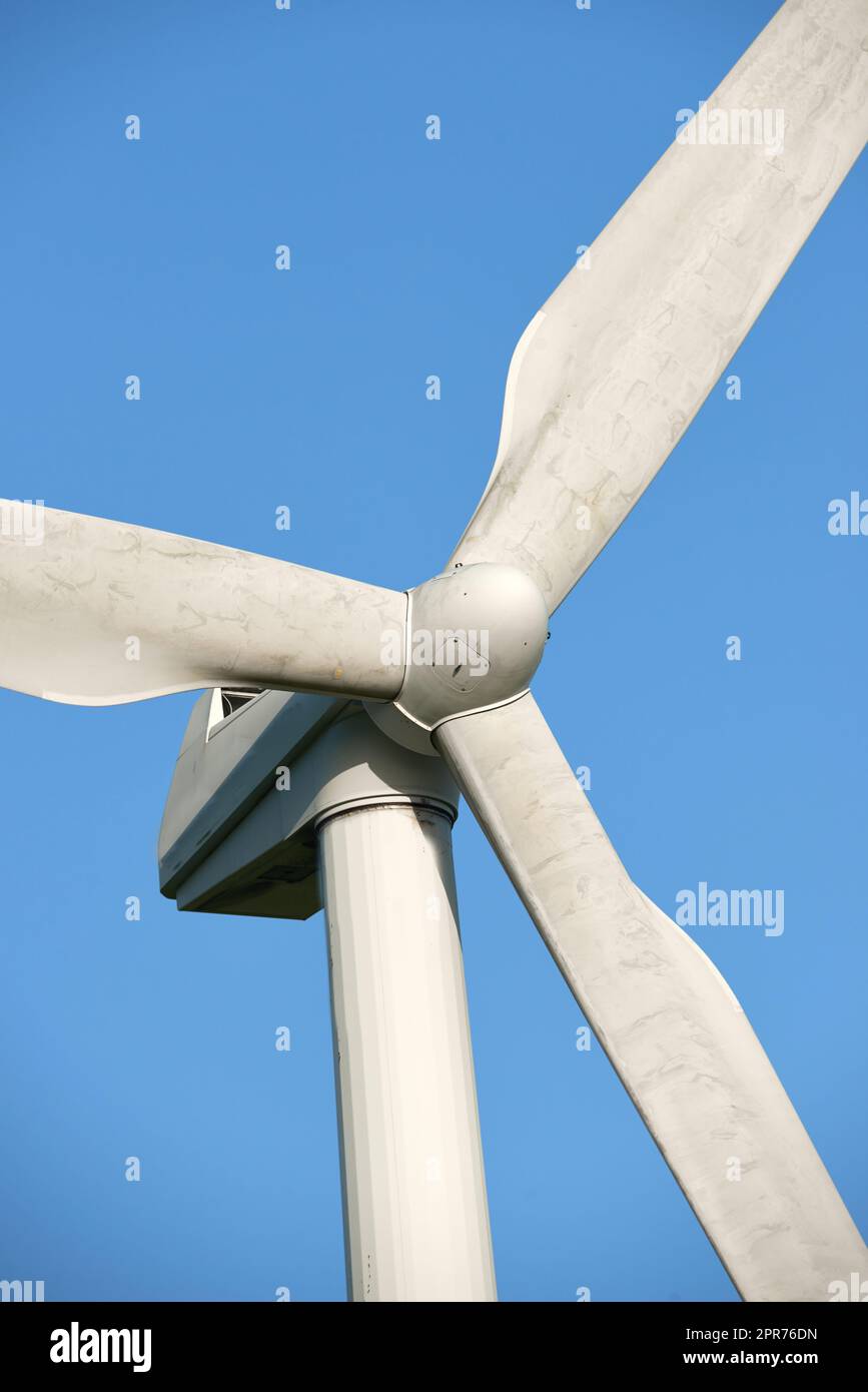 Eine Windturbine und Rotorschaufeln, die gegen den blauen Himmel auf einem nachhaltigen, umweltfreundlichen Hof isoliert sind. Niederwinkelansicht der Gewinnung einer biologisch abbaubaren Energiequelle zur Erzeugung von Strom aus windigen Klimazonen Stockfoto