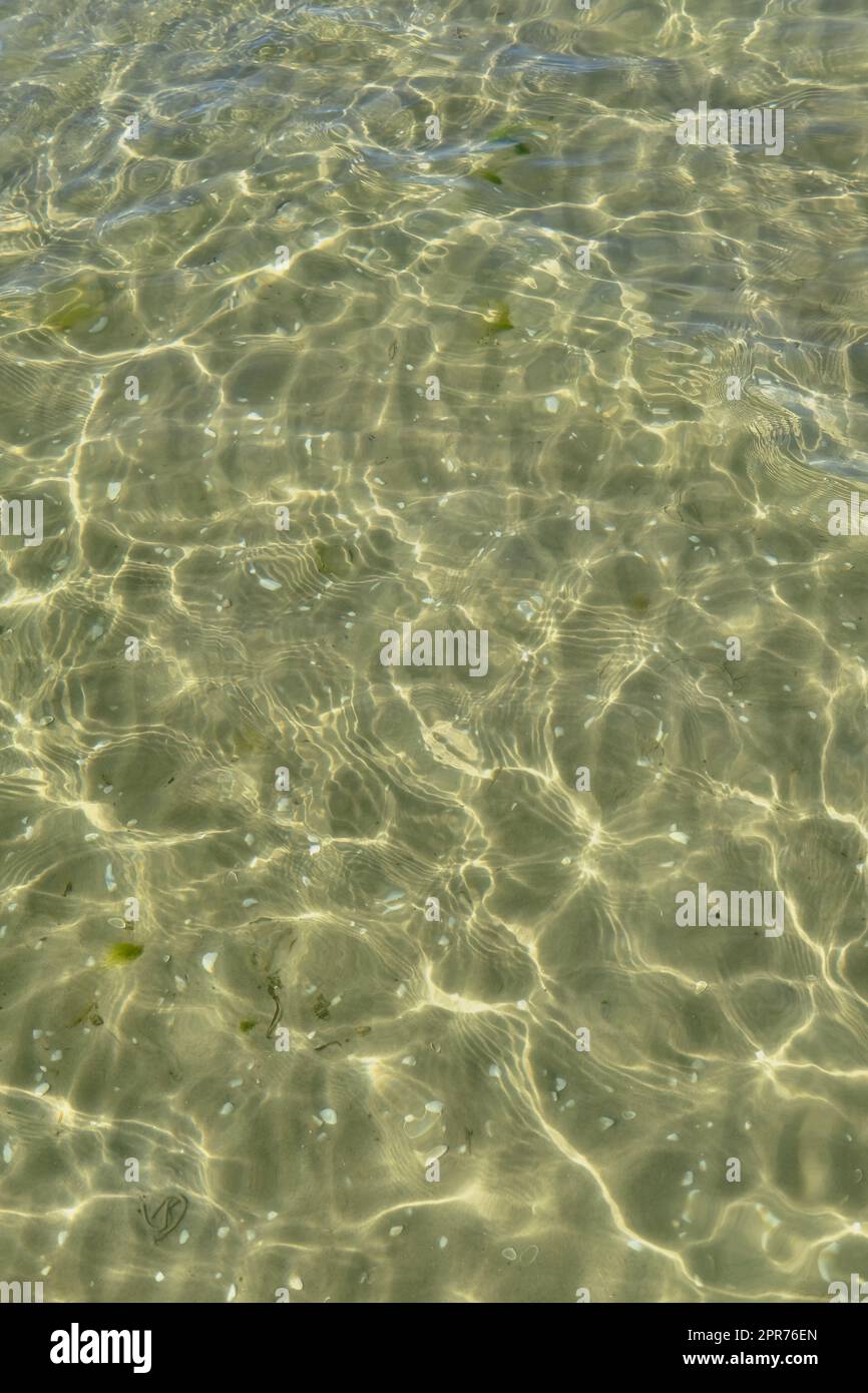 Blick über das Sonnenlicht, das vom Wasser am Strand reflektiert wird, mit Kopierbereich. Flache Wellen und ruhige Wellen an der Küste an sonnigen Tagen draußen. Klare, flüssig brechende Sonnenstrahlen vor Sommerhintergrund Stockfoto