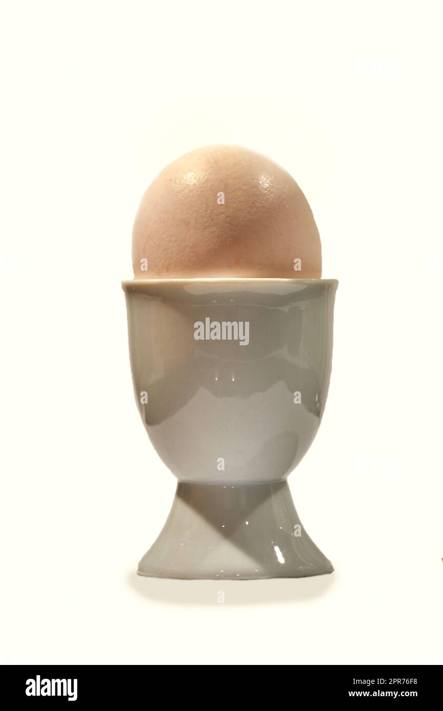 Nahaufnahme eines gekochten Eies in einem keramischen Becherhalter isoliert vor cremefarbenem Hintergrund mit Kopierraum. Diät, gesunde Proteine essen in der Morgenmahlzeit Routine und Frühstück. Eier unterstützen die Muskelsynthese Stockfoto