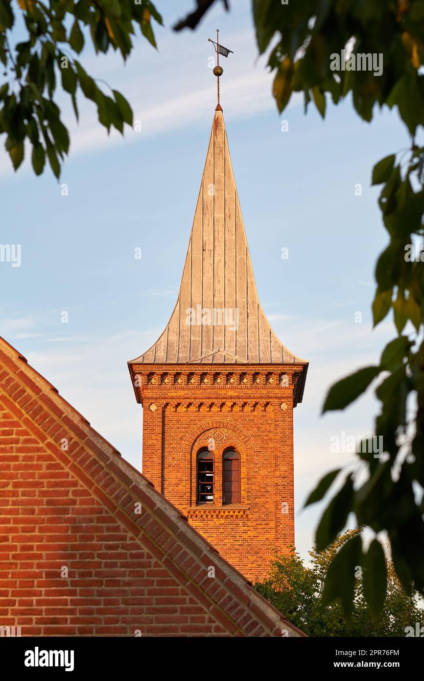 Der niedrige Winkel eines Kirchenglockenturms vor einem blauen Himmel. Außenansicht eines traditionellen alten religiösen roten Backsteingebäudes an einem sonnigen Tag. Wand und Dach eines historischen Hauses oder Wohnarchitektur-Design Stockfoto