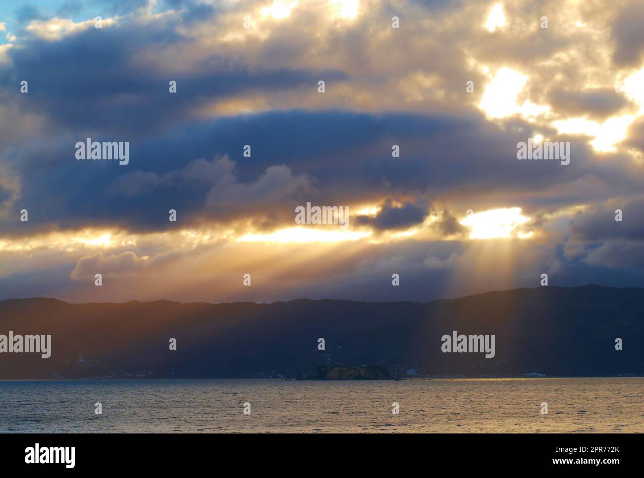 Sonnenlicht durchbricht dunkle Wolken über einem ruhigen Ozean. Sonnenlicht, das am frühen Morgen durch dicke Wolken scheint. Lichtstrahlen, die einen Durchbruch machen, durch schwere, erstickende Wolken Stockfoto