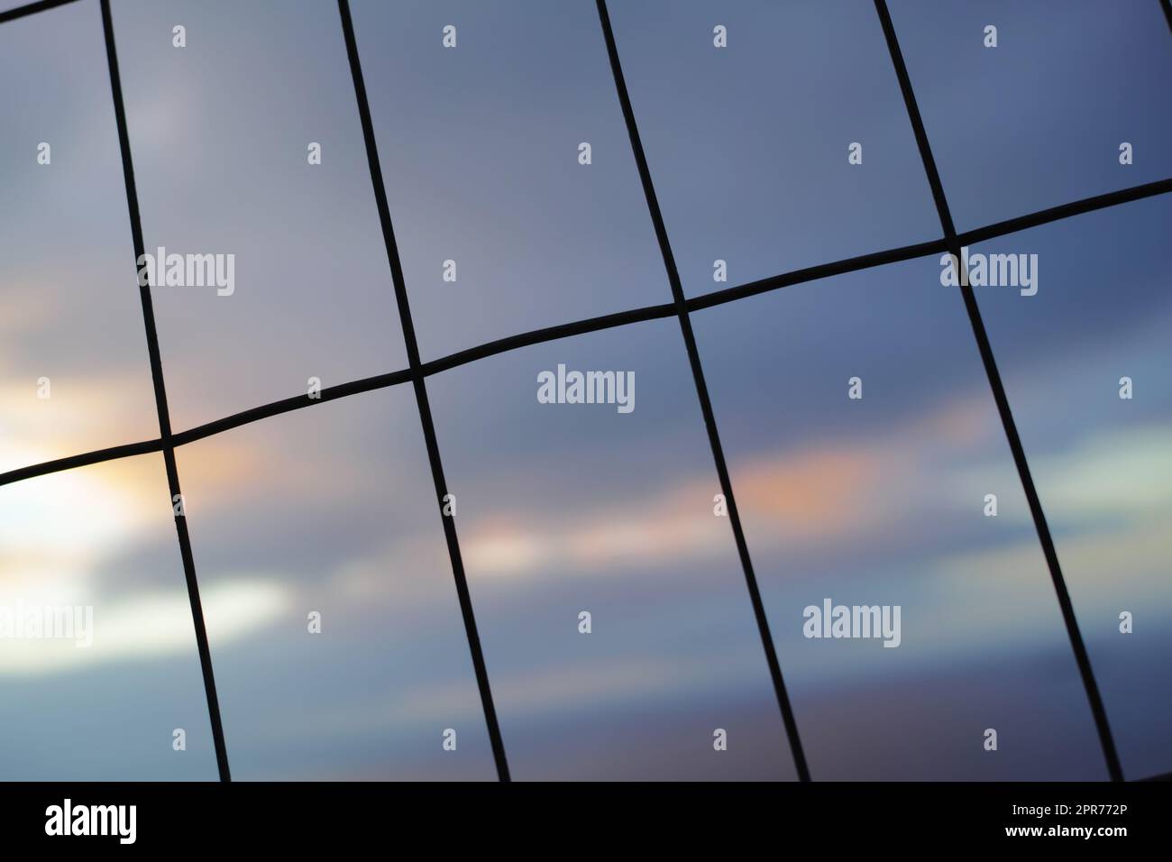 Eisenzaun in vertikalen, horizontalen Linien vor einem unscharfen Himmelshintergrund. Draht in rechteckigen Formen für ein Sicherheits- oder Sicherheitskonzept. Die Textur von Fenstermustern oder dunklen Silhouetten eines Anschnitts Stockfoto