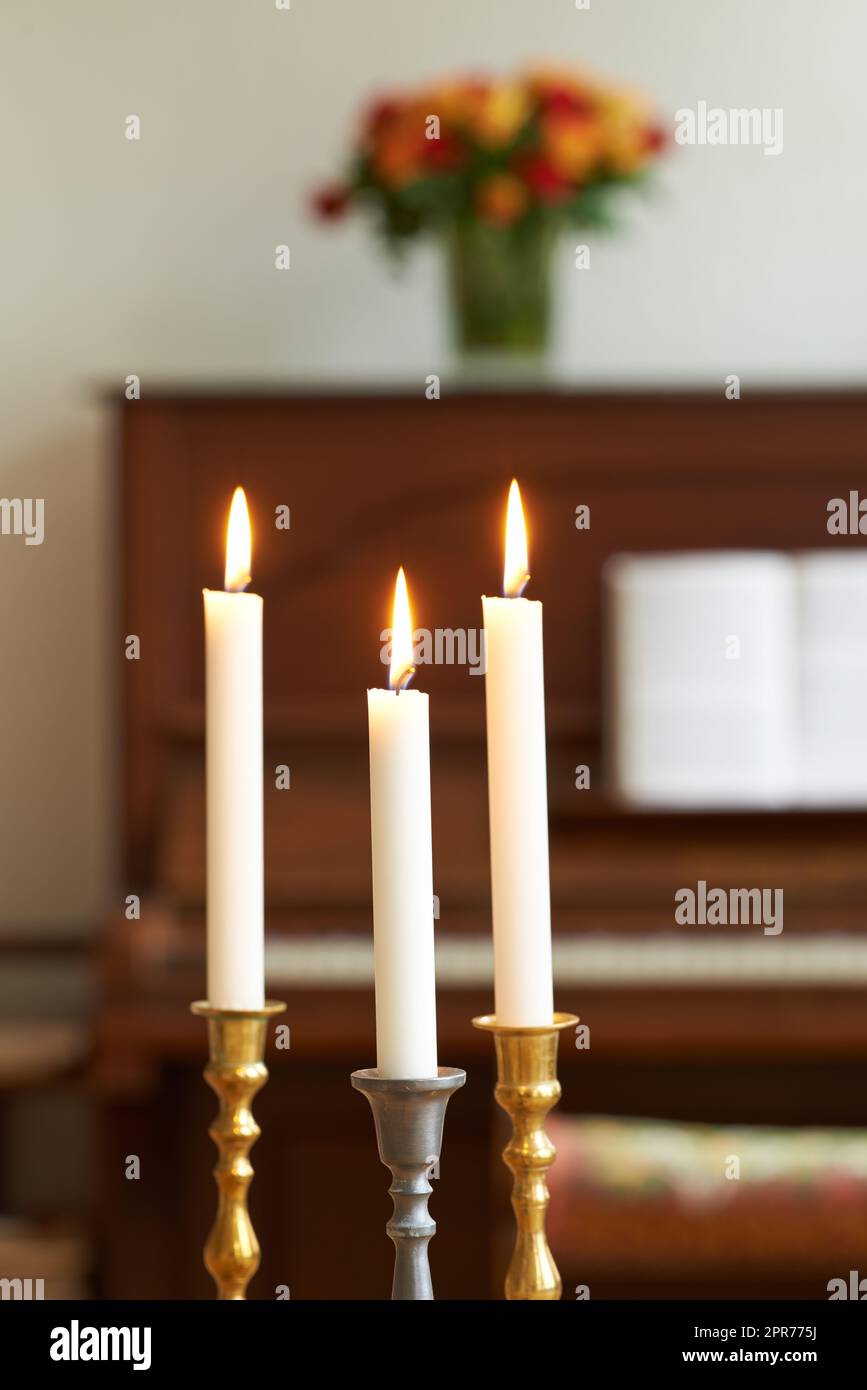 Brennende Kerzen in einem gemütlichen Raum vor einem verschwommenen Hintergrund. Das Anzünden einer Kerze symbolisiert Hoffnung und Glauben an die Religion. Kerzen in Gold- und Silberhaltern, für eine Hochzeit, ein Bestattungsinstitut oder eine Kirche Stockfoto