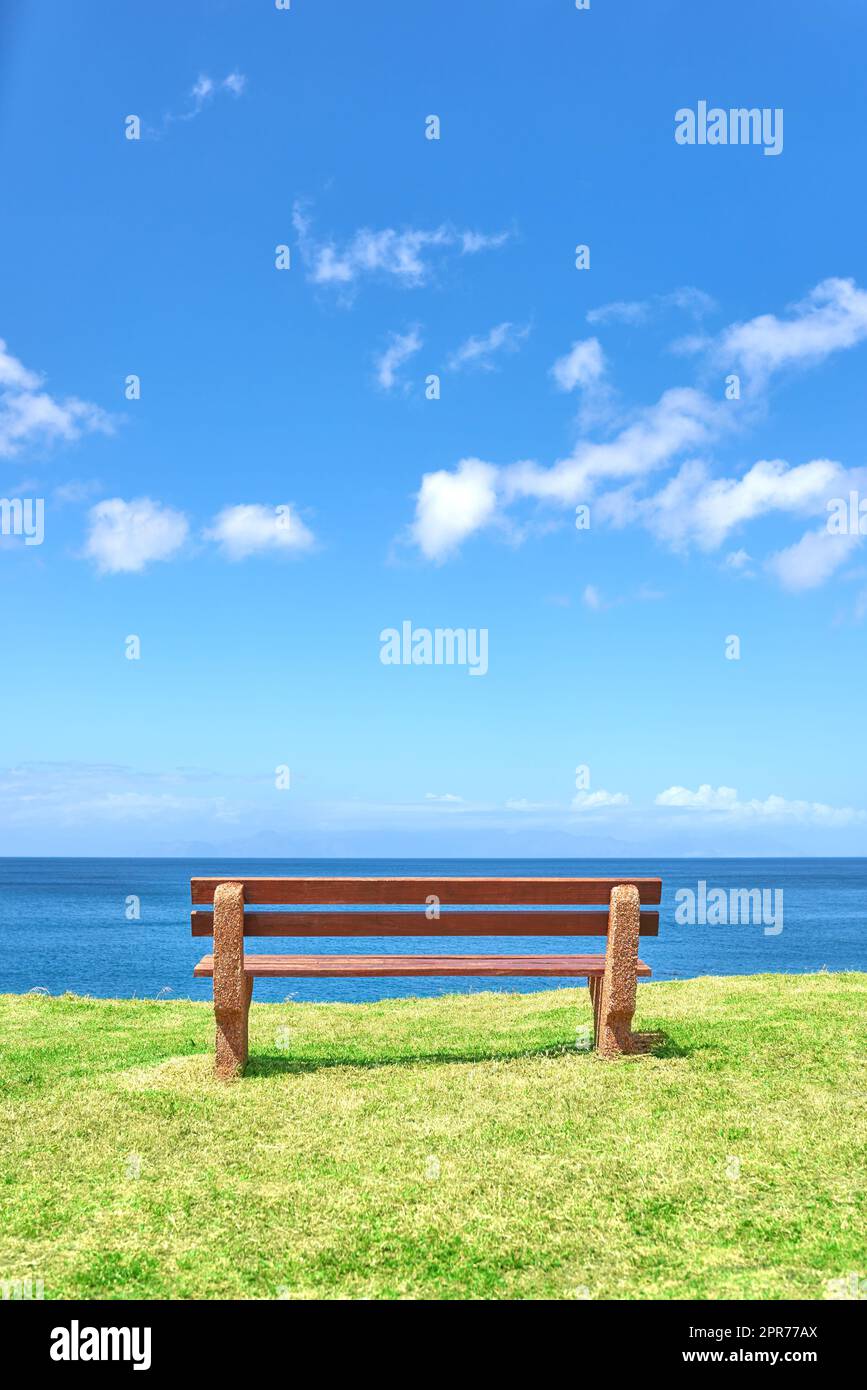 Wunderschöner Blick auf den Strand von einer Bank mit Kopierbereich an einem Sommertag mit blauem Hintergrund. Friedliche und ruhige Meereslandschaft mit einem Sitz in einem Küstenurlaubsort. Landschaftlich reizvolle Meeres- oder Meeresküste Stockfoto