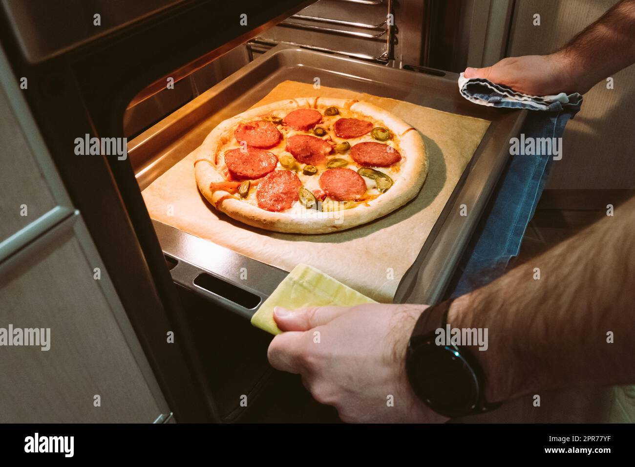 Ein Mann zieht zu Hause ein Tablett mit Peperoni-Pizza aus dem Ofen Stockfoto