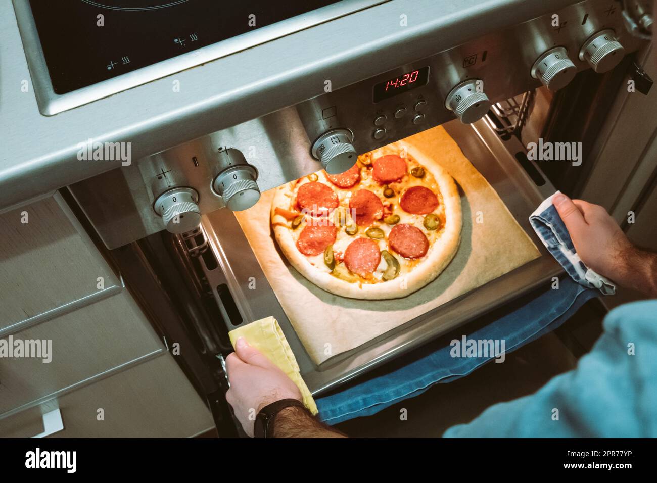 Erhöhte Sicht auf Herrenhände, die eine fertige hausgemachte Pizza aus dem Ofen ziehen Stockfoto