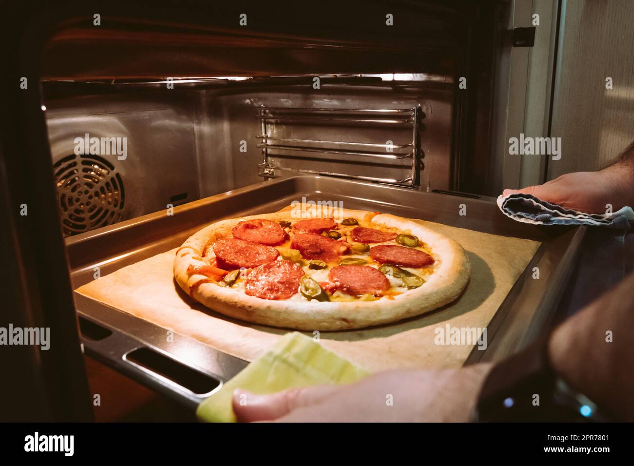 Die Hände eines Mannes ziehen eine hausgemachte Peperoni-Pizza aus dem Ofen Stockfoto