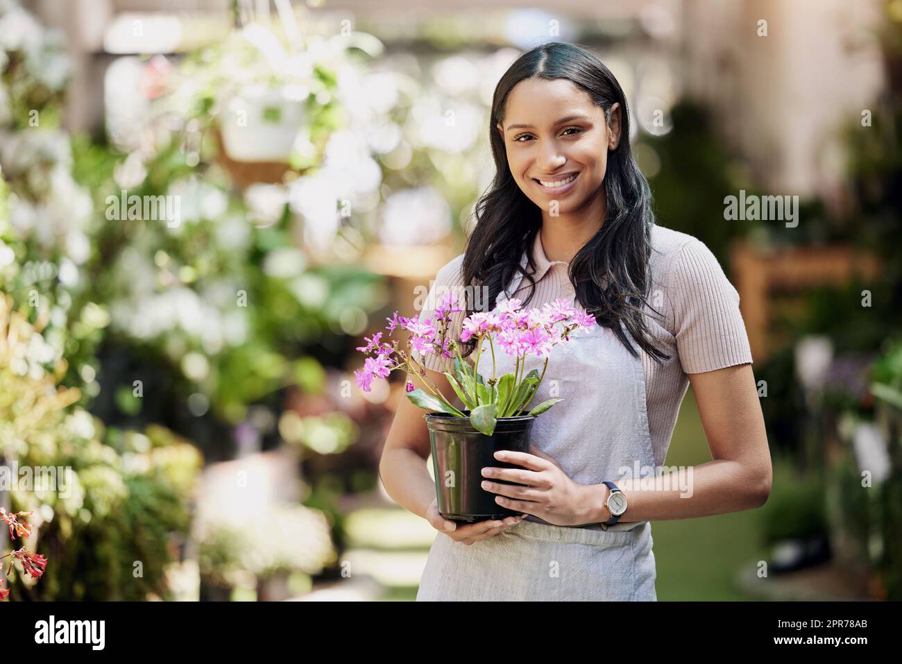 Dame der Blumen. Porträt eines jungen Geschäftseigentümers, der eine Topfpflanze in einer Gärtnerei hält. Stockfoto