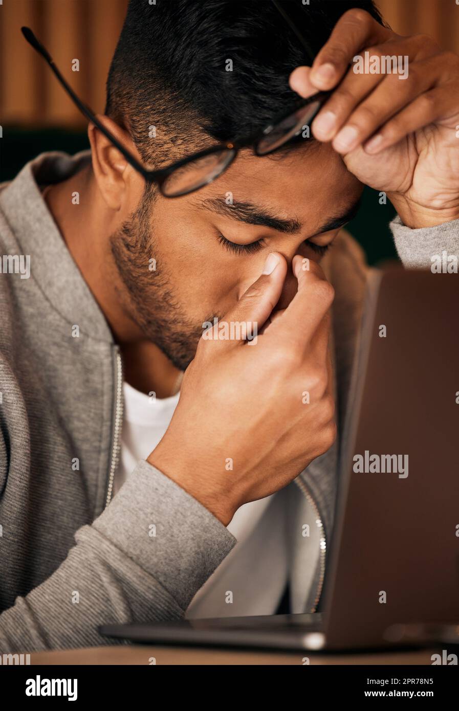 Nahaufnahme eines jungen indianers, der sich gestresst fühlt, während er allein sitzt und ein Laptop zum Surfen im Internet benutzt. Mischrassen-Schüler mit Kopfschmerzen im späten Nachtschichten. Fehler machen Stockfoto