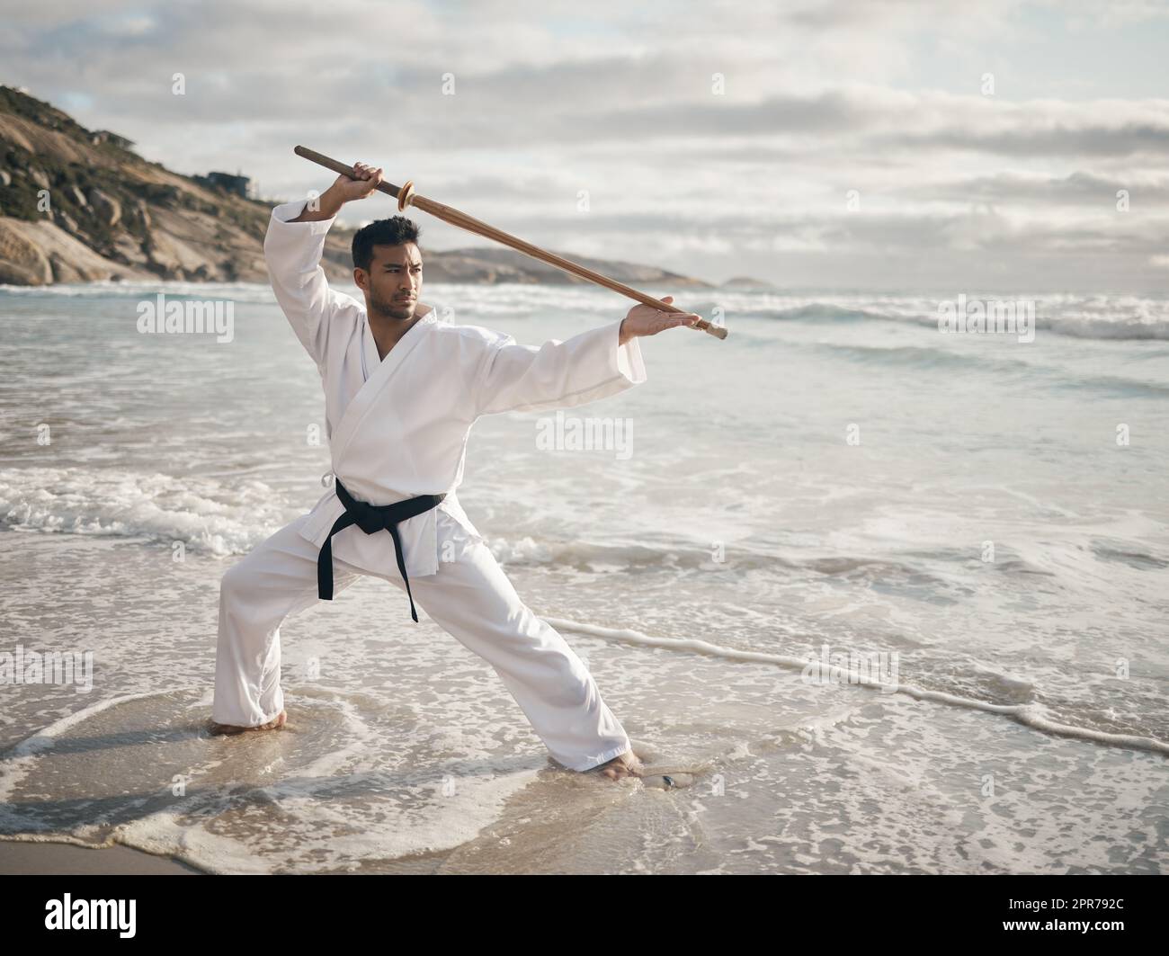 Bojustu. Ganzkörperaufnahme eines hübschen jungen männlichen Kampfkünstlers, der am Strand Karate übt. Stockfoto
