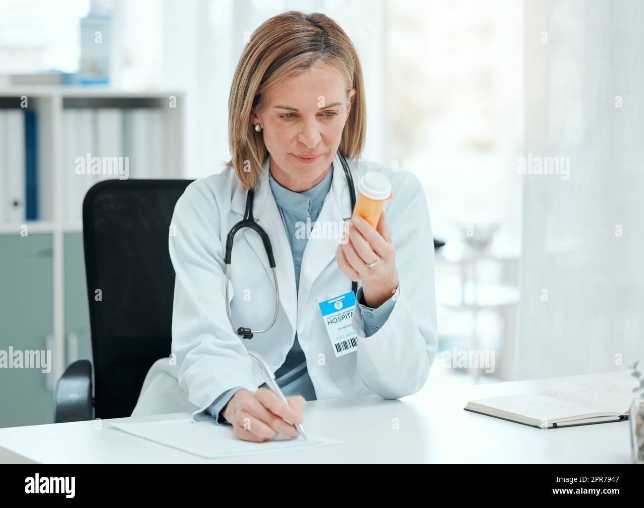 Dies sind die besten Pillen für meinen Patienten. Aufnahme einer reifen Ärztin, die allein in ihrer Klinik sitzt und Notizen schreibt, während sie eine Flasche Pillen in der Hand hält. Stockfoto