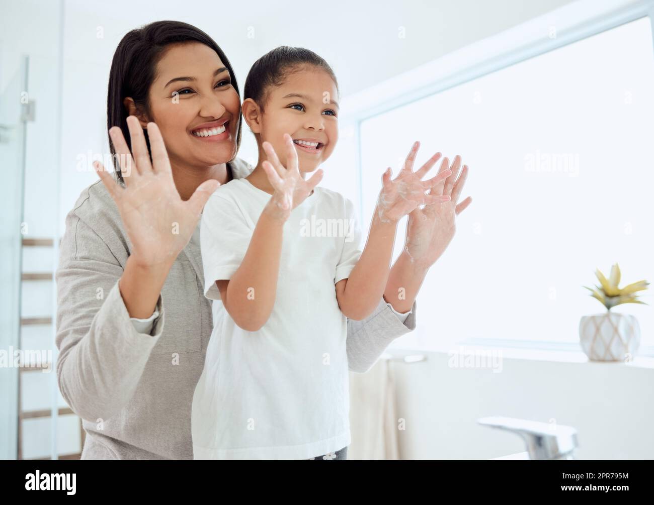 Wir bedeckten jeden Finger. Aufnahme eines entzückenden kleinen Mädchens, das sich die Hände wäscht, während ihre Mutter zu Hause hilft. Stockfoto