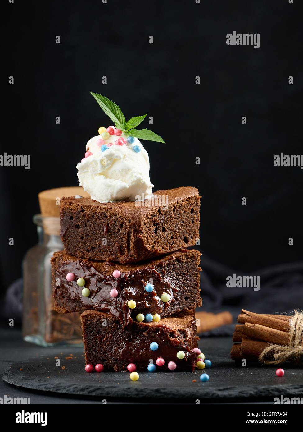 Gebackene Brownie-Schokoladenstückchen auf einem schwarzen Tisch, auf einer Kugel Eis Stockfoto