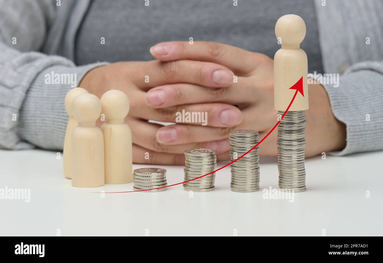 Ein Stapel Metallmünzen und hölzerne Figuren von kleinen Männern, die nach oben zeigen. Steigende Lebensmittelpreise Stockfoto