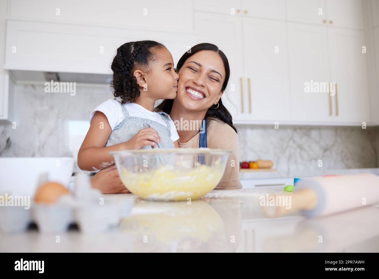 Mutter und Tochter backen zusammen in einer Hausküche. Ein fürsorgliches kleines, bezauberndes Mädchen, das ihre alleinerziehende Mutter auf die Wange küsst. Glückliche Frau und liebevolles Kind, das sich innen anfreundet und kochen lernt Stockfoto