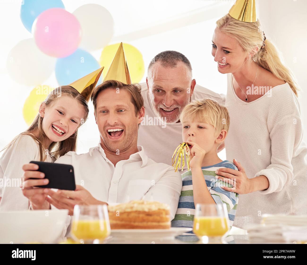 Eine glückliche Familie feiert einen Geburtstag mit einer Party, trägt Hüte und macht ein Selfie am Telefon. Reifer Mann, der auf einer Party ein Foto von Vater, Frau und Kindern macht und dabei besondere Erinnerungen weckt Stockfoto