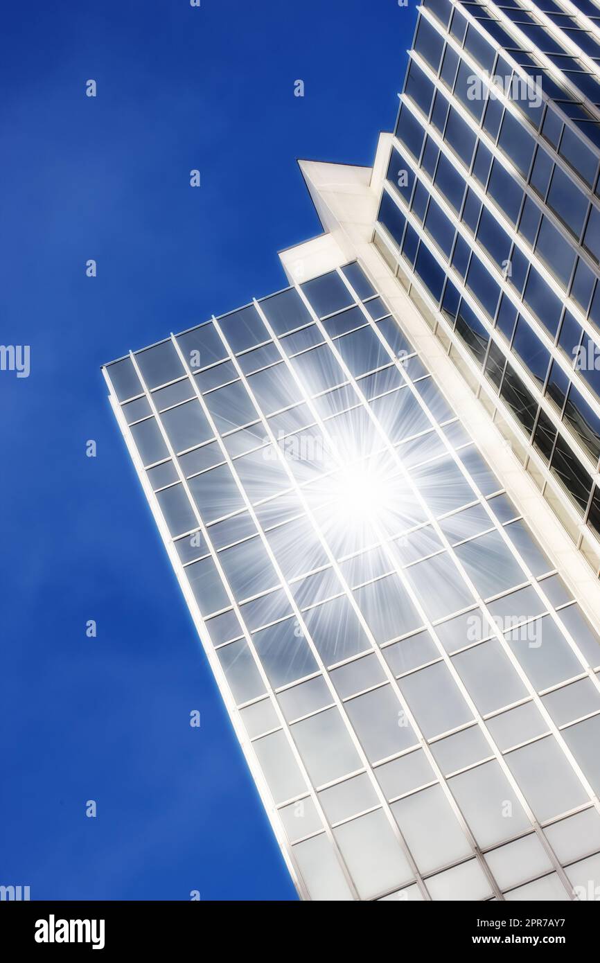 Geometrische Glasfenster auf einem Wolkenkratzer, bei denen die Sonne ein Linsenlicht vor einem blauen Hintergrund von unten reflektiert. Äußere architektonische Details eines modernen und hohen Hochhauses in der Stadt Stockfoto