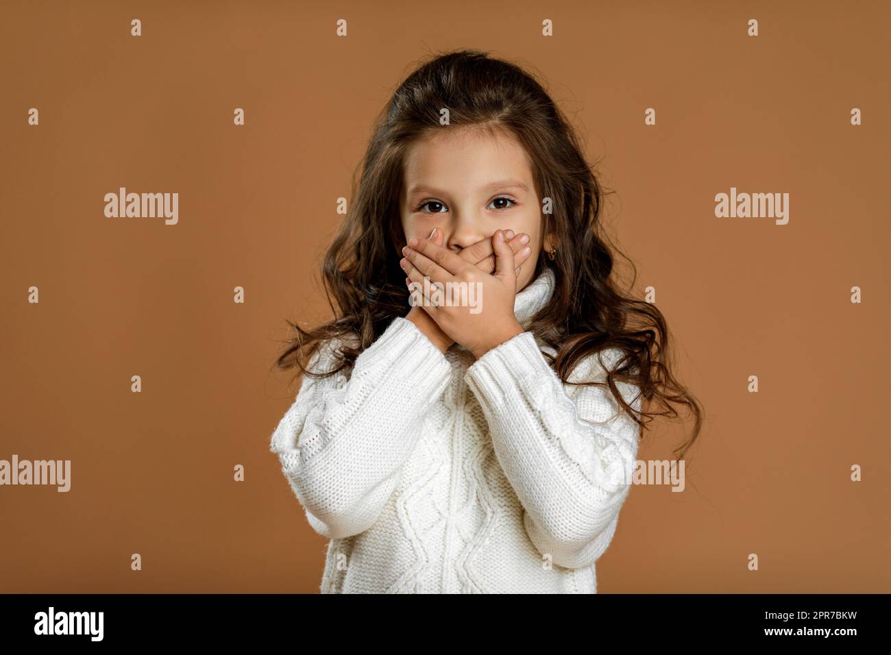 Ein wunderschönes, lockiges Mädchen im weißen Pullover, das um Ruhe bittet. Stockfoto