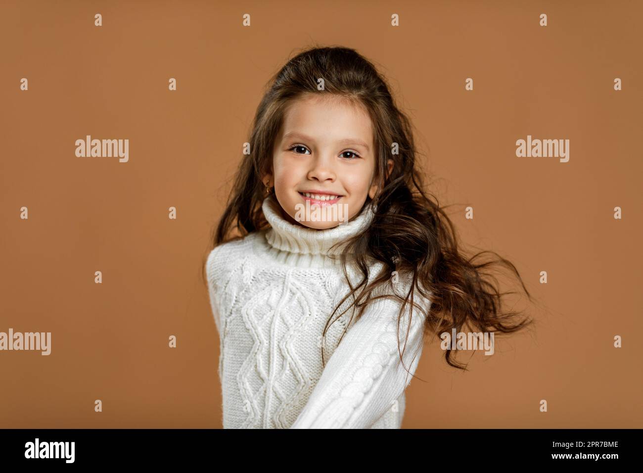 Ein kleines Mädchen im weißen Pullover, das in die Kamera schaut Stockfoto