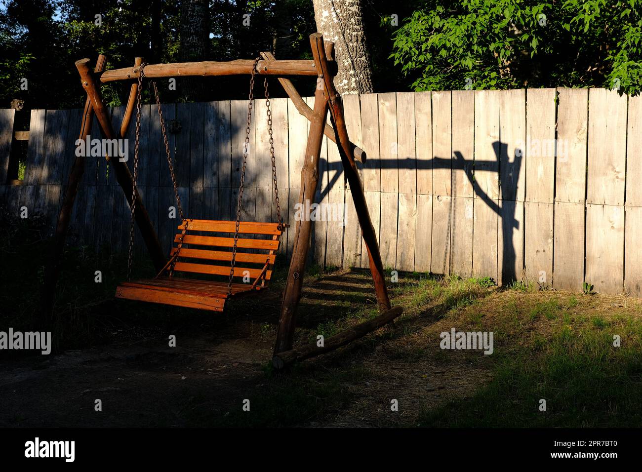 Schwingen Sie an einem sonnigen Tag eine Holzbank in einem Garten. Stockfoto