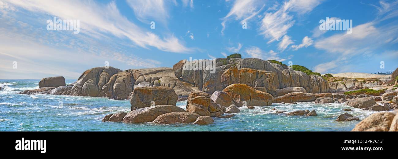 Panoramablick auf Camps Bay, Kapstadt, Südafrika mit Felsen, Felsen und blauem Himmel mit Kopierbereich. Ozeane Wellen, die sich auf einen rauen, felsigen Strand ziehen. Reisen und Tourismus im Ausland und im Ausland Stockfoto