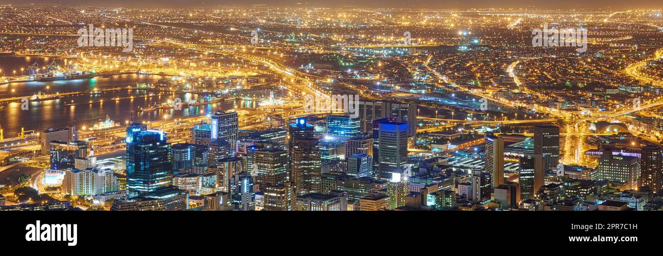 Weitwinkel einer Stadt bei Nacht von oben. Futuristisches Panorama der Lichter von Kapstadt bei Sonnenuntergang. Eine moderne städtische Landschaft einer beleuchteten Stadt. Blick von Signal Hill in Südafrika Stockfoto