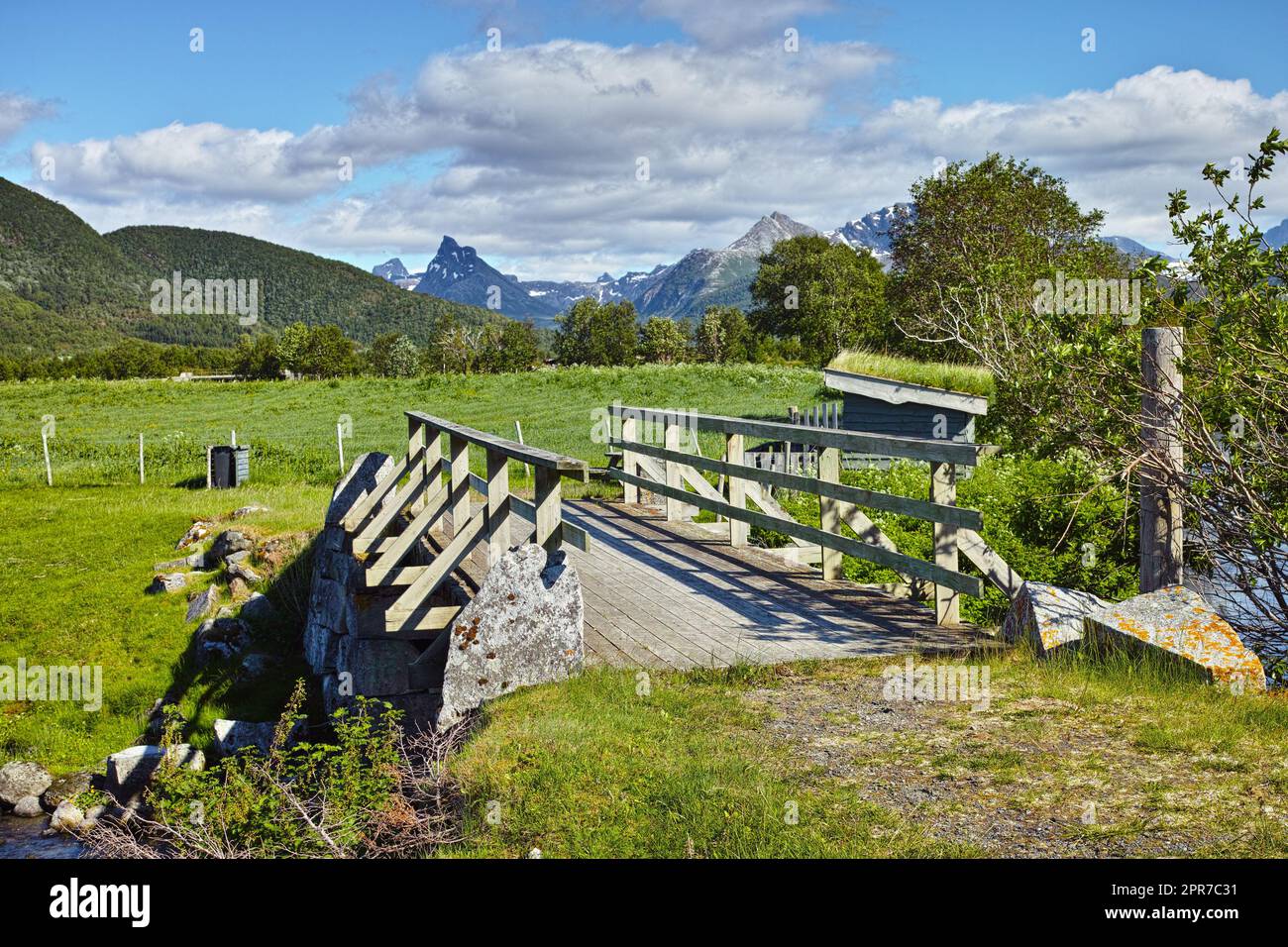 Landschaft mit Holzbrücke in abgelegener grüner Landschaft von Bodo in Nordland, Norwegen. Infrastruktur und gebaute Kreuzung in ökologischen Wiesen und Umweltfeldern. Erkunden Sie die Natur während des Tages Stockfoto