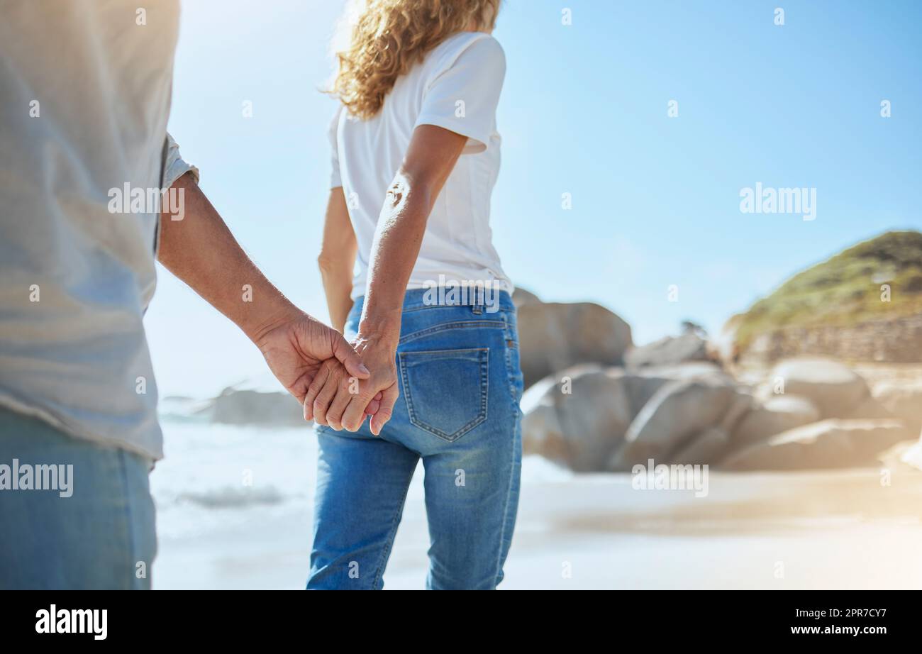 Nahaufnahme eines liebevollen, erwachsenen Paares, das Händchen hält, während er im Sommer am Strand spaziert. Liebevoller Mann und Frau, die im Urlaub am Meer spazieren gehen. Mann und Frau auf einem entspannten Date Stockfoto