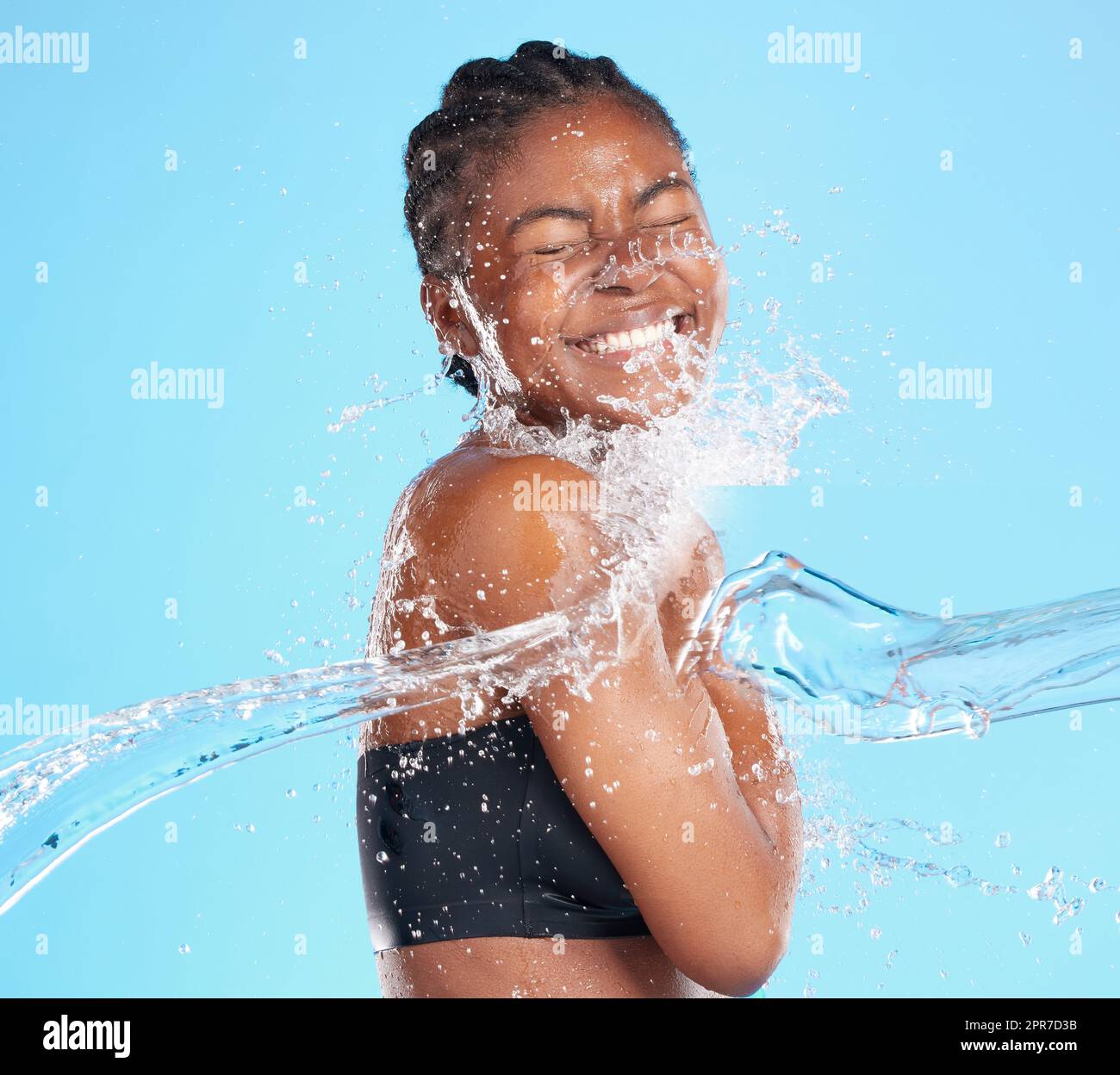 Ihr Lächeln ist Sonnenschein. Aufnahme einer schönen jungen Frau, die vor blauem Hintergrund mit Wasser bespritzt wurde. Stockfoto