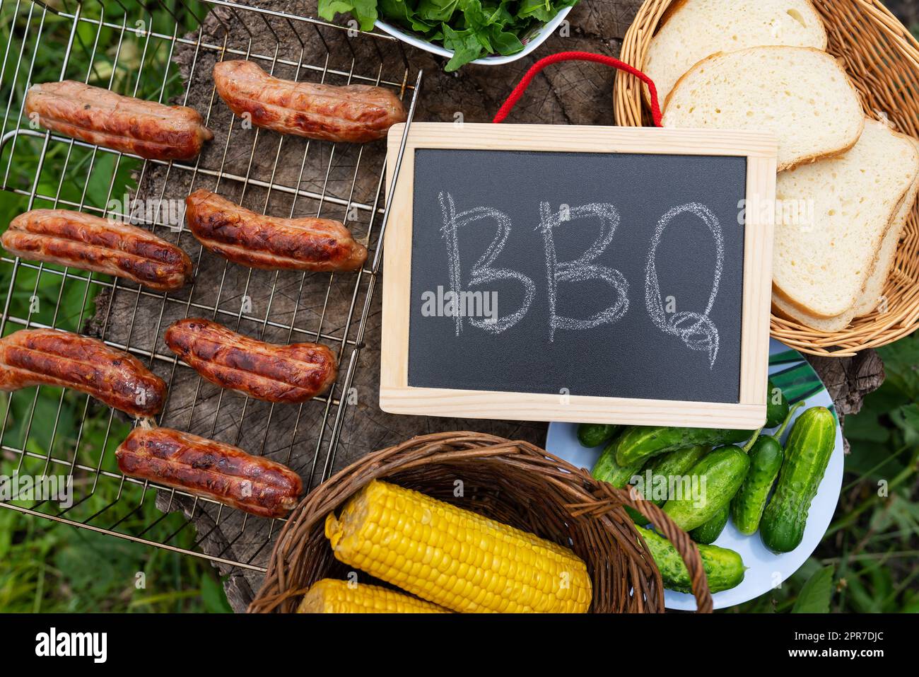 Barbecue-Aufschrift auf der Tafel, gegrillte Würstchen, Mais, Brot. Freizeitaktivitäten im Freien. Stockfoto