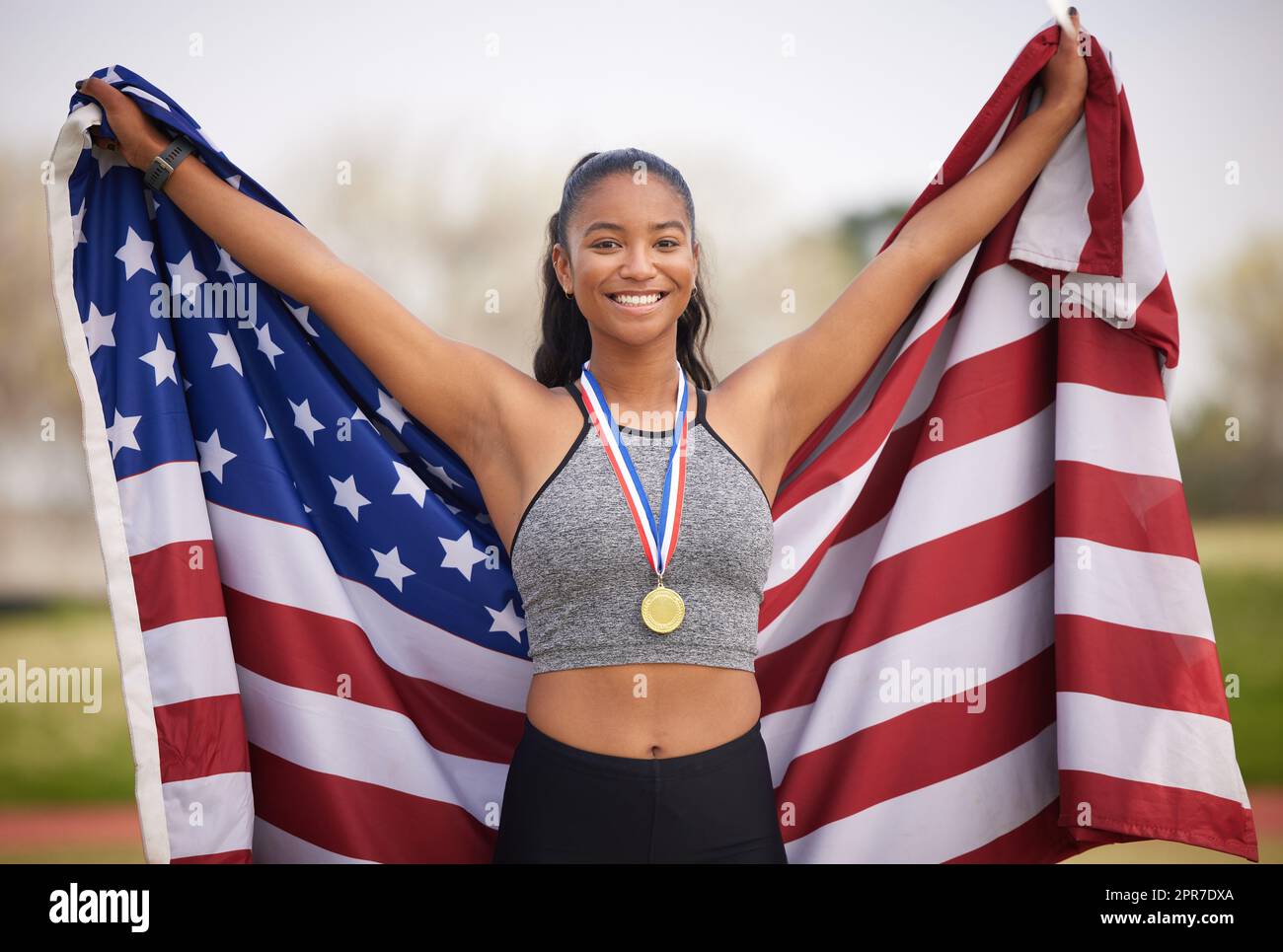 Heben Sie Ihre Fahne. Beschnittenes Porträt einer attraktiven jungen Sportlerin, die einen Sieg für ihr Land feiert. Stockfoto